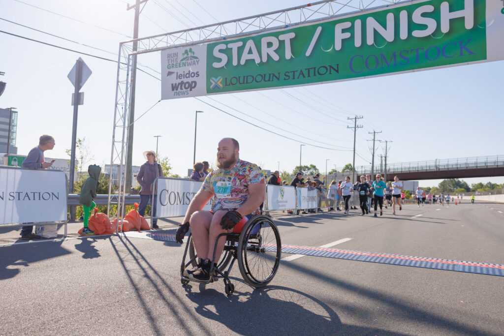 Anthony Ringenberg from the Ability Fitness Center at The Arc of Loudoun team is the first
wheelchair user across the finish line at Run the Greenway in 2023. (Swim Bike Run Photo)